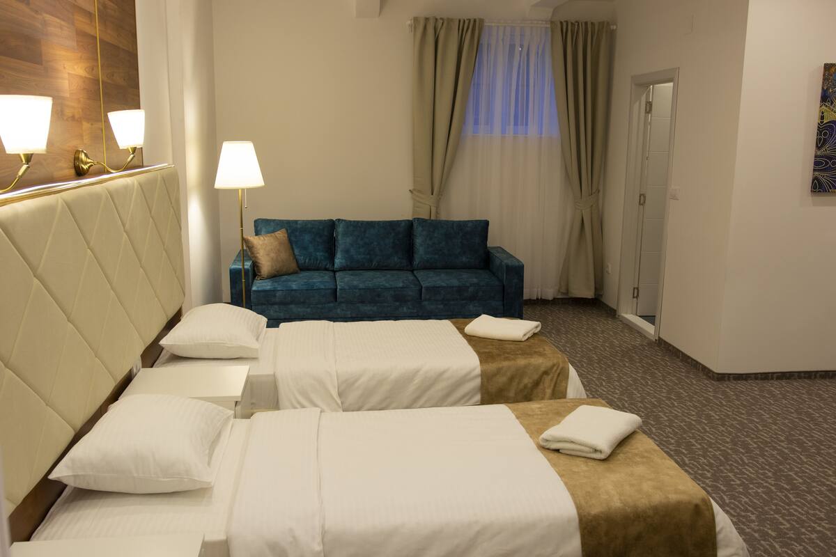 Habitación de hotel con dos camas, un sofá azul, un espejo con apliques de pared y un cuadro en la pared.