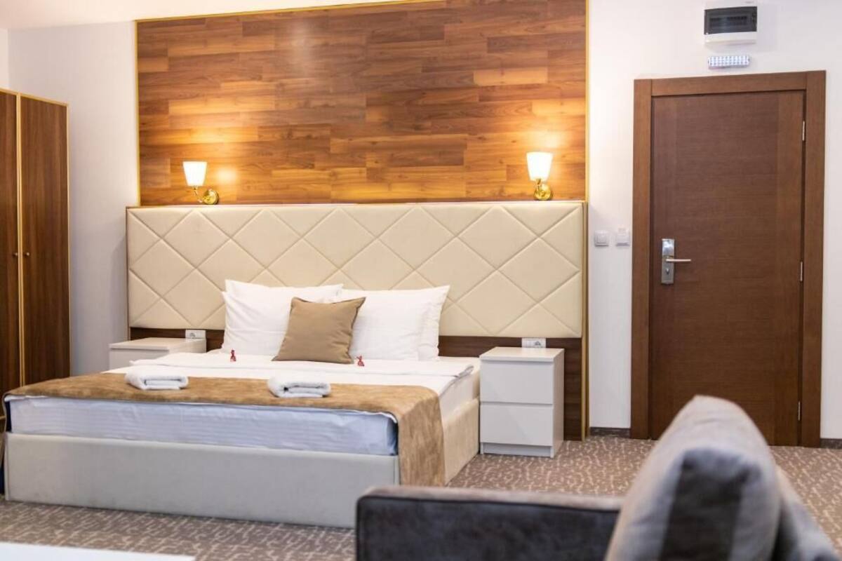 Una habitación de hotel con una cama grande, mesitas de noche, un cabecero de madera y una puerta.