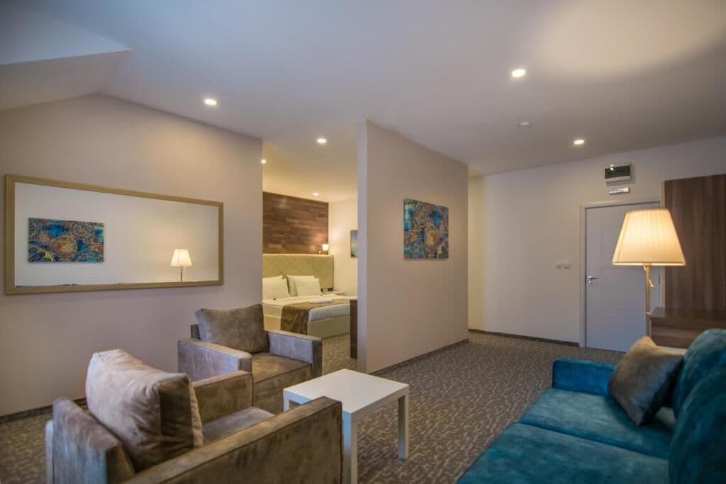 A hotel room with a bed, a sitting area with a sofa and armchairs, a small table, and artwork on the walls.