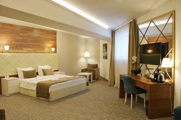 Une chambre d’hôtel comprenant un lit, des tables de chevet, un bureau avec une chaise, une télévision et un grand miroir.
