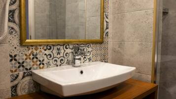 Une salle de bain avec un lavabo blanc, un miroir à cadre doré et des carreaux décoratifs sur le mur.