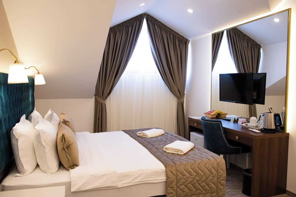 Una habitación de hotel con cama, escritorio, televisor y ventana con cortinas.