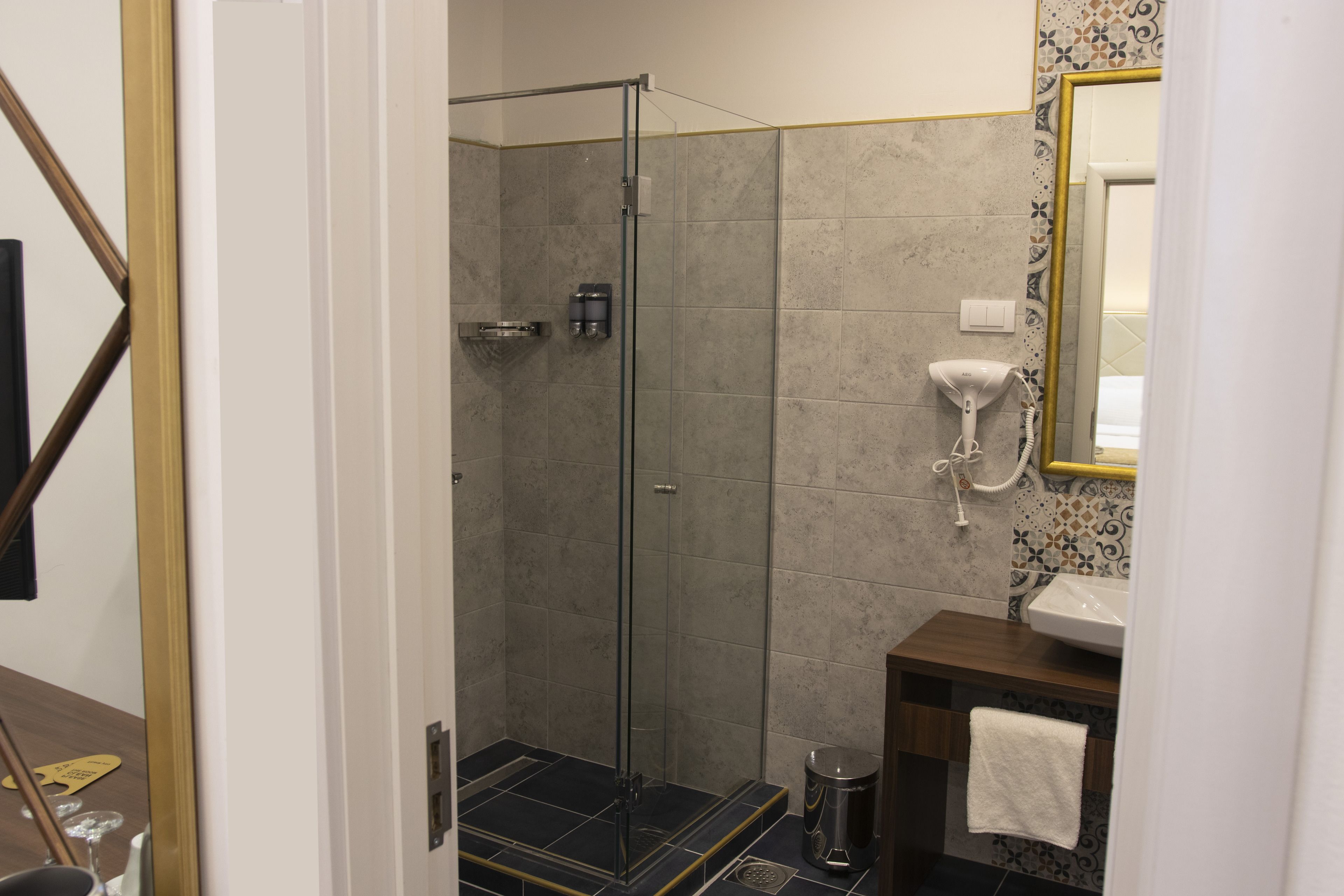 A modern bathroom with a glass-enclosed shower, a white sink, and a mirror with a gold frame.