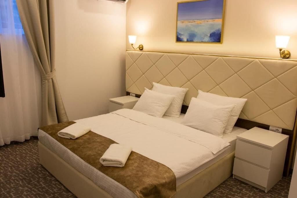 A hotel room with a bed, two bedside tables, a headboard, and a painting on the wall.