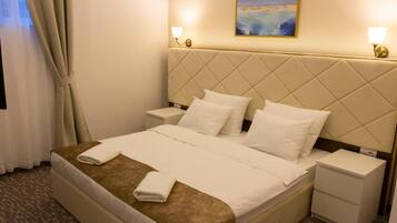 A hotel room with a bed, two bedside tables, a headboard, and a painting on the wall.