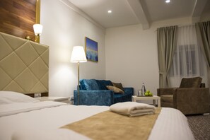 Une chambre d’hôtel avec un lit, un canapé bleu, un fauteuil marron, une petite table avec une lampe et un tableau au mur.