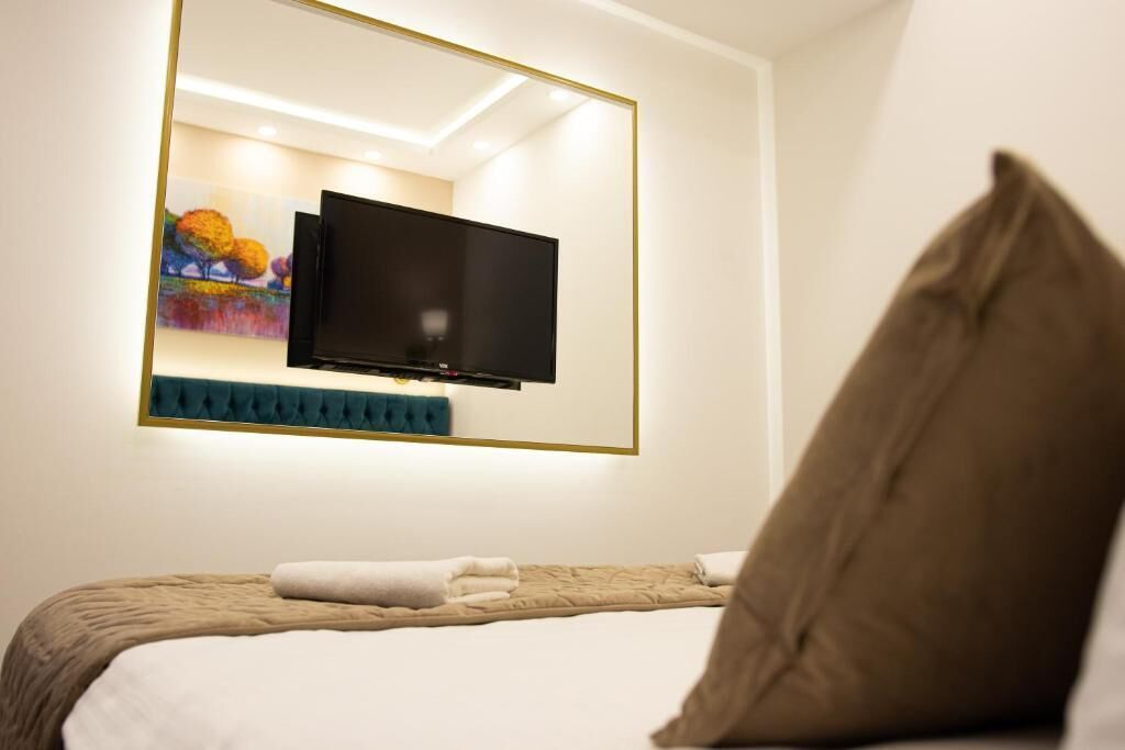 A hotel room with a bed, a flat-screen TV mounted on the wall, and a painting above the TV.