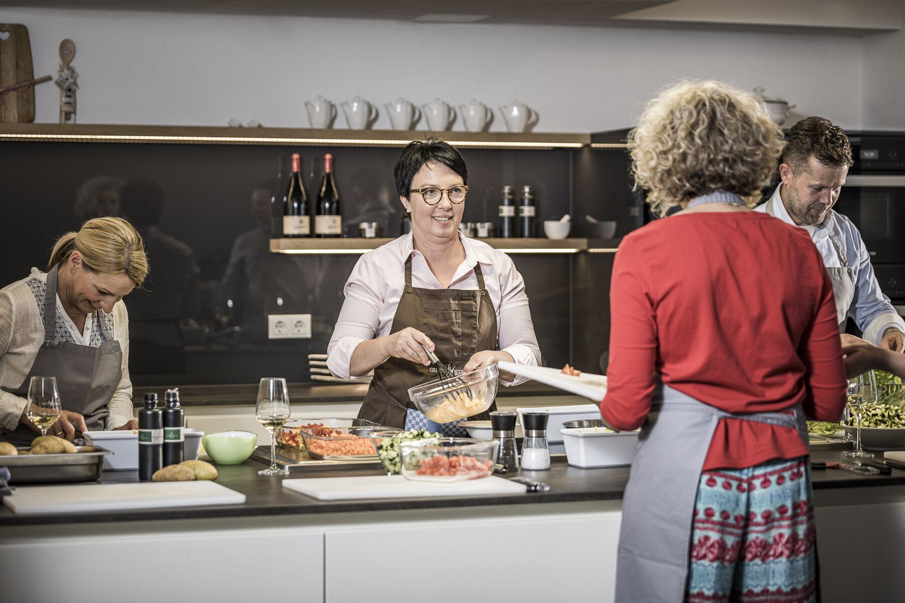 Una cocina con un chef preparando comida, una mesa de buffet con diversos platos y una alacena para vinos al fondo.
