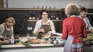 A kitchen with a chef preparing food, a buffet table with various dishes, and a wine rack in the background.