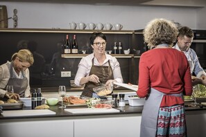 Una cocina con un chef preparando comida, una mesa de buffet con diversos platos y una alacena para vinos al fondo.