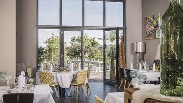 A dining area with tables set for two, large windows, and a view of the outdoors.