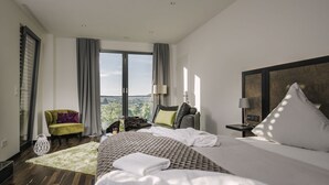 A modern hotel room with a large bed, a sofa, a chair, and a view of the outdoors. - Genusswerk Eifel - Boutique Hotel (Korperich)