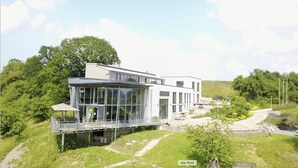 A modern building with large glass windows, a flat roof, and a small outdoor area with a pathway. - Genusswerk Eifel - Boutique Hotel (Korperich)
