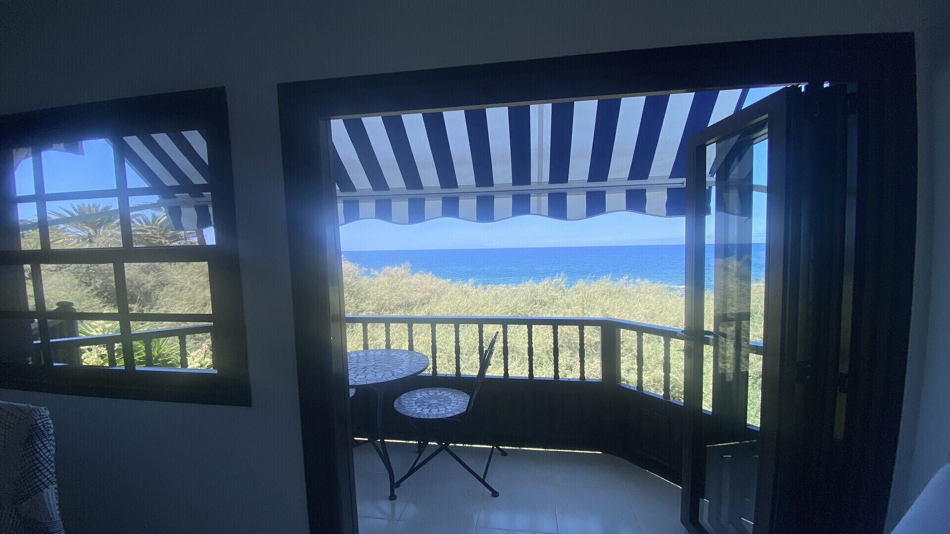 A balcony with a view of the ocean, a small table, and a chair.