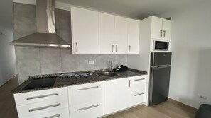 Una cuina moderna amb armaris blancs, una campana extractora d'acer inoxidable, un microones integrat i un frigorífic.