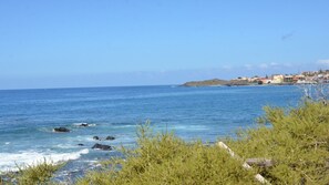 Vista della costa con acqua cristallina, un litorale roccioso e un paese in lontananza con edifici.