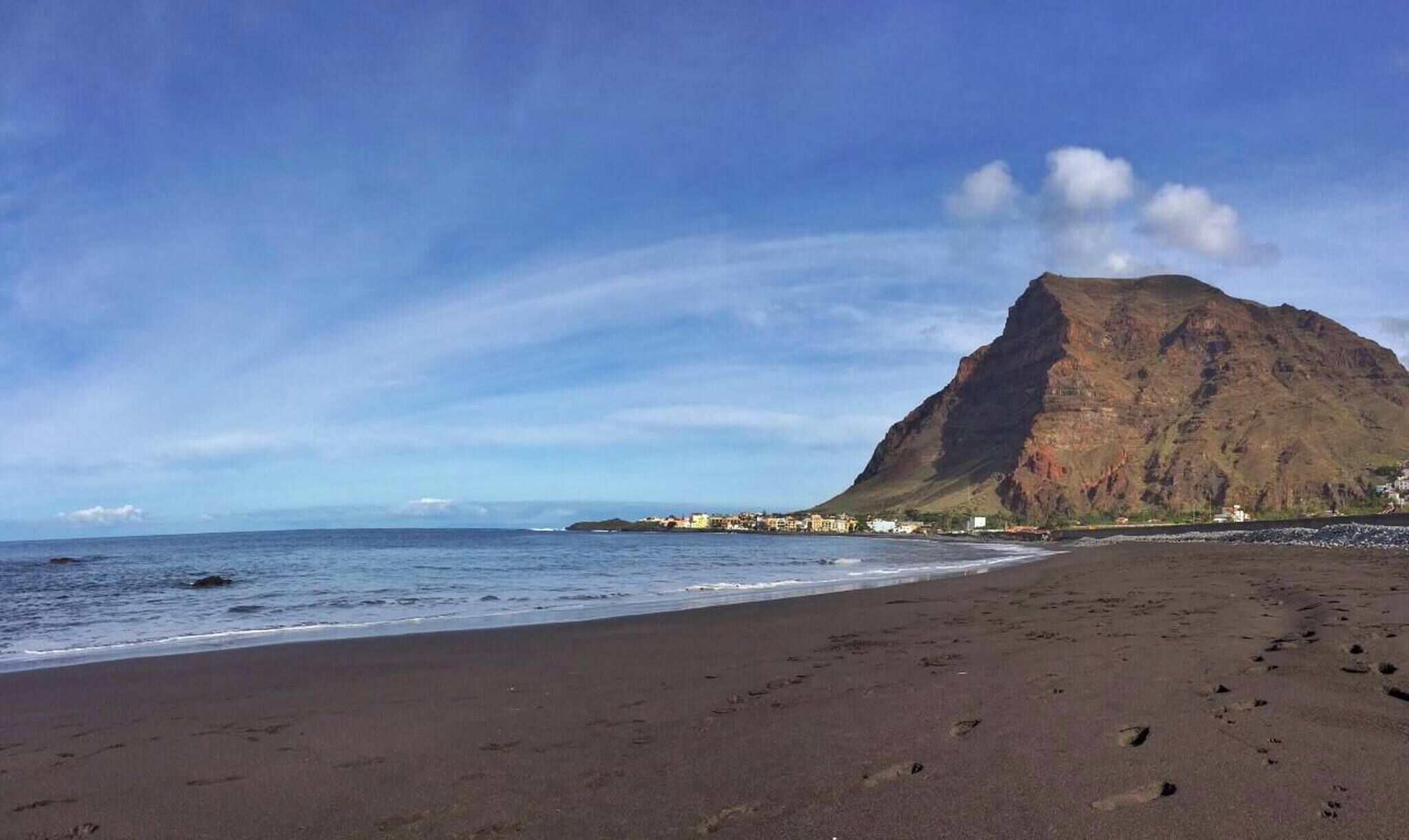 A beach with a prominent mountain in the background, a clear sky, and a calm sea.