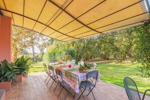 Enjoy al fresco dining in a serene garden setting, surrounded by lush greenery and a shaded patio.