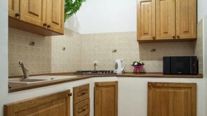 Cocina pequeña con muebles de madera, microondas, tetera y lavamanos.