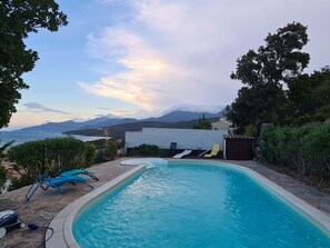 Une piscine avec des chaises longues, une vue sur la mer et des montagnes en arrière-plan.