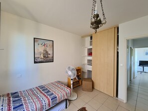 Une chambre à coucher comprenant un lit, un ventilateur, une armoire et une porte donnant sur une autre pièce.