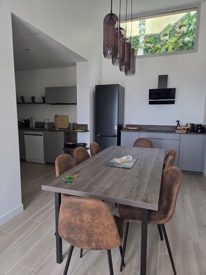 A modern kitchen with a dining area, a built-in oven, and a large window with a view of greenery.