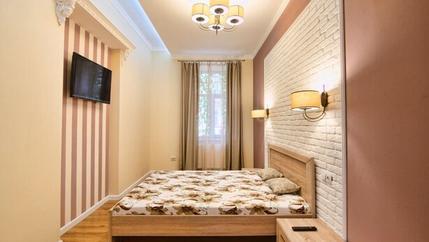 A bedroom with a wooden bed, a television on the wall, a brick accent wall, and a chandelier. - Apartment Kostushka 5 (Lviv)