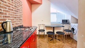 A compact kitchen with a brick wall, a gas stove, a microwave, and a washing machine. - Apartment Kostushka 5 (Lviv)