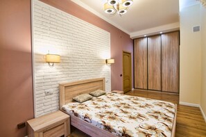A bedroom with a brick-patterned wall, a wooden bed, two wall-mounted lamps, and a wardrobe. - Apartment Kostushka 5 (Lviv)