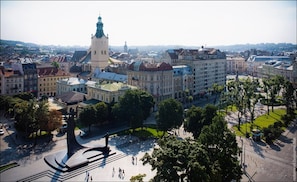 Un paisaje urbano con edificios históricos, una torre destacada y una plaza central con una fuente.