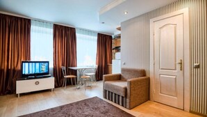 Una sala de estar moderna con televisor, sofá, mesa de comedor con sillas y un amplio ventanal con cortinas.