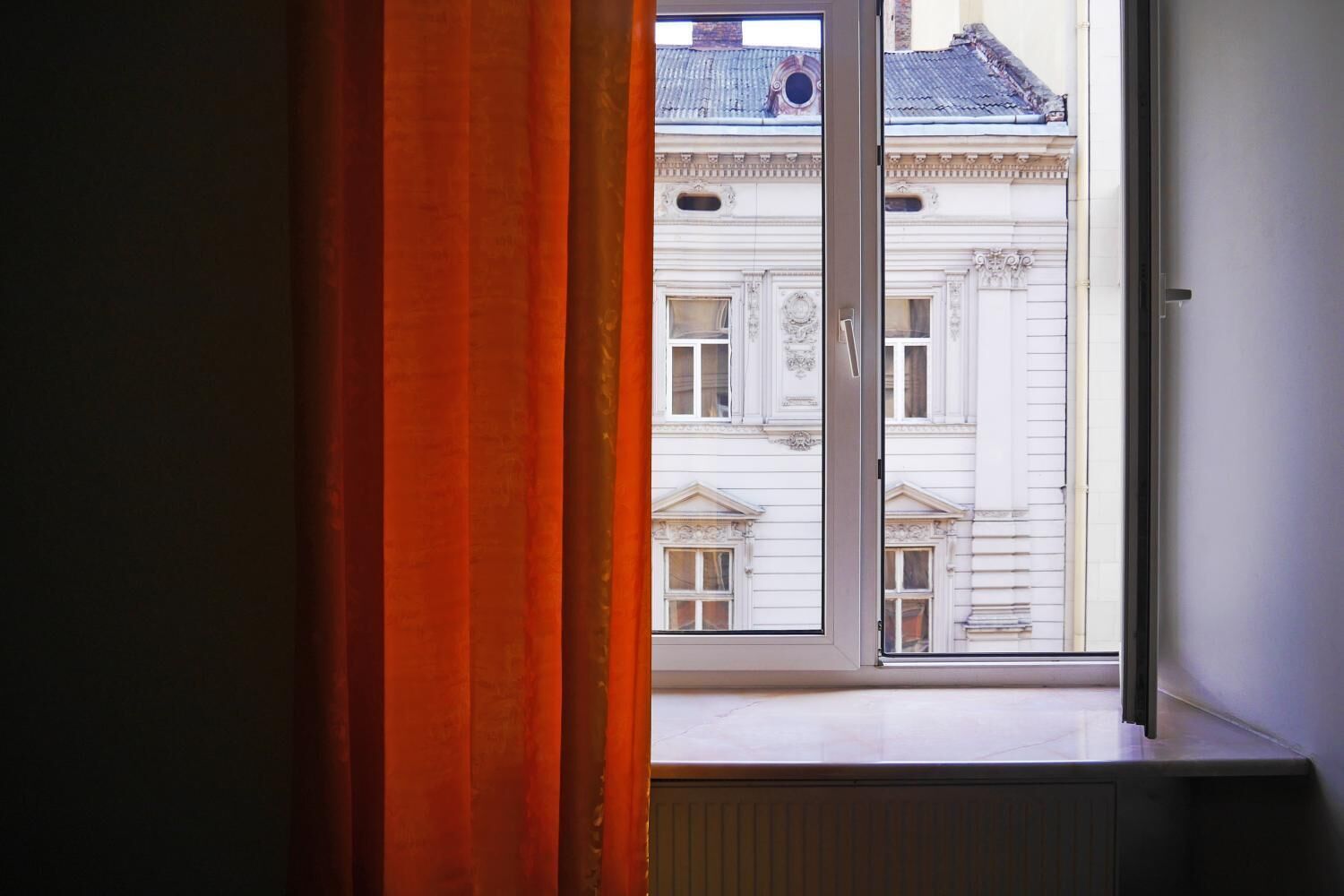 Een raam met uitzicht op een gebouw in klassieke architectuur, met decoratieve details en een balkon.