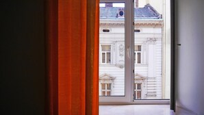 Una ventana con vista a un edificio de arquitectura clásica, con detalles ornamentales y un balcón.