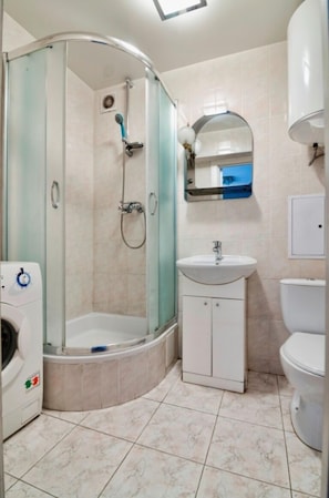 Un baño con ducha de vidrio, lavamanos, inodoro y lavadora.