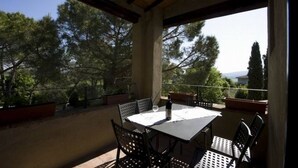 Un patio cubierto al aire libre con una mesa y sillas, con vistas a un paisaje escénico con árboles y vista al mar.