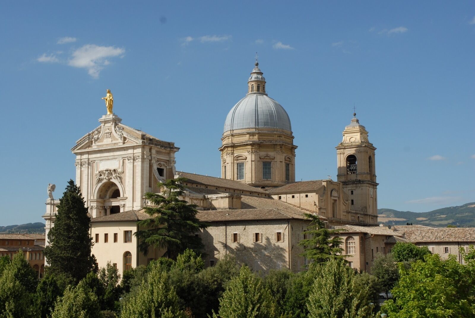 Un edificio storico con una cupola imponente e un campanile, circondato da lussureggiante vegetazione.