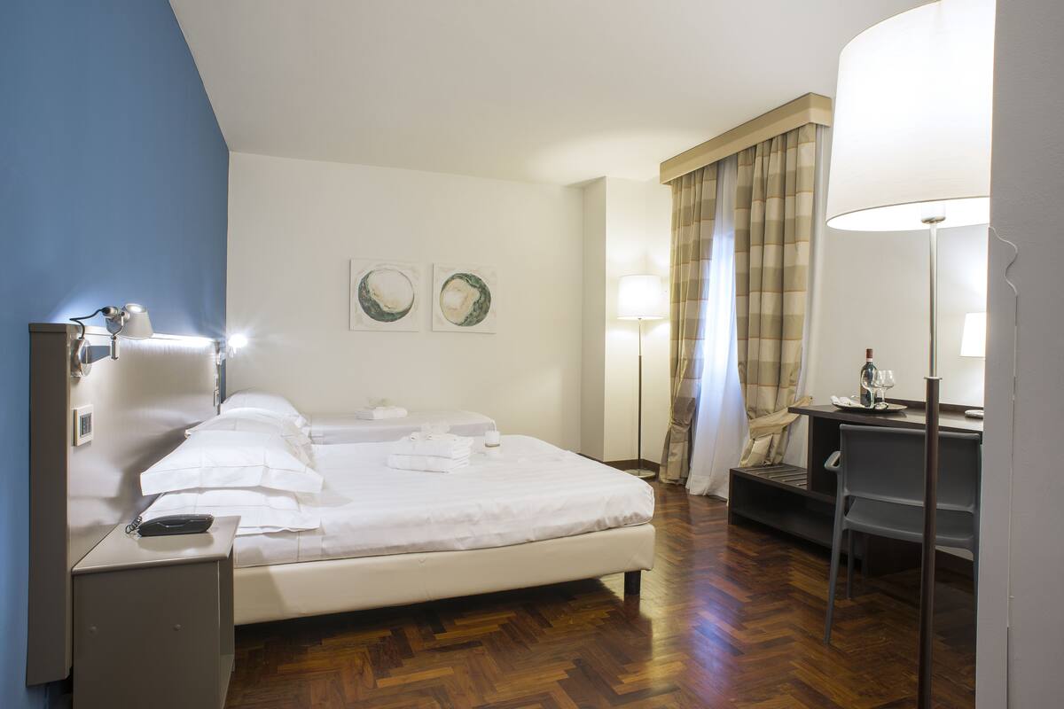 Une chambre d’hôtel comprenant un lit, une table de chevet, une lampe, un bureau, une chaise et des rideaux.