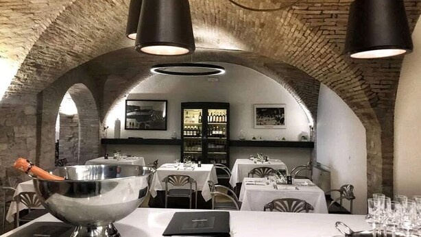 A restaurant with arched brick ceilings, white tablecloths, and black pendant lights. - Locanda Giustini (Assisi)
