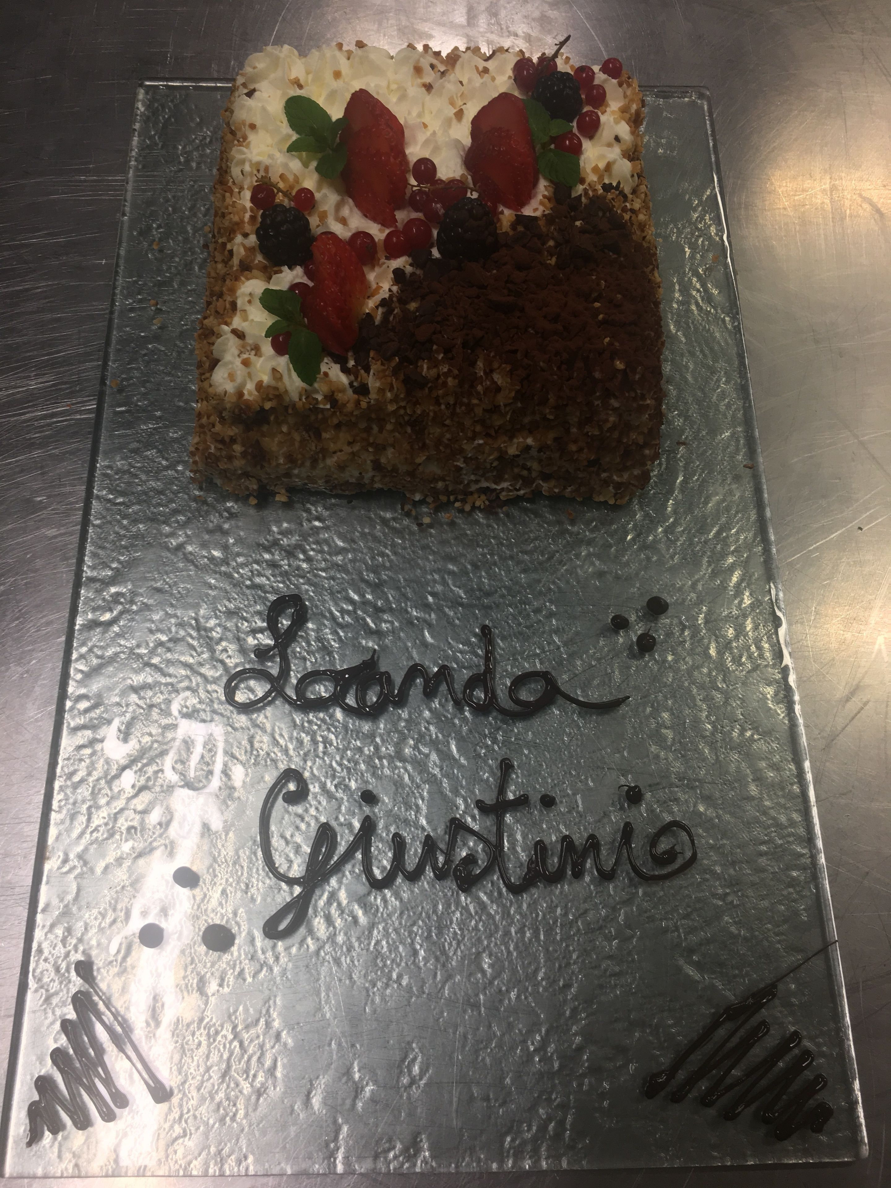 Uma fatia de bolo com fruta sobre um suporte de bolo de prata. O suporte tem a inscrição 'La Marta: Giustino'.