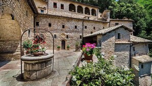 A stone building with a courtyard, featuring a central fountain and potted plants. - Locanda Giustini (Assisi)