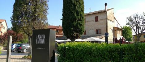 Señal de 'Locanda Giustini', con un camino de grava, coches aparcados y un edificio con contraventanas rojas al fondo.