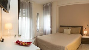 Quarto de hotel com uma cama grande, mesas de cabeceira com abajures, uma escrivaninha com luminária e uma TV montada na parede.