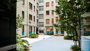 Um pátio com piso de azulejos, plantas em vasos e um edifício com várias janelas e varandas.