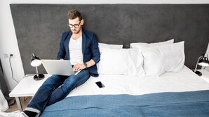 A person sitting on a bed with a laptop, a smartphone, and a lamp on a bedside table. - Apartment Horodotska 4 (Lviv)