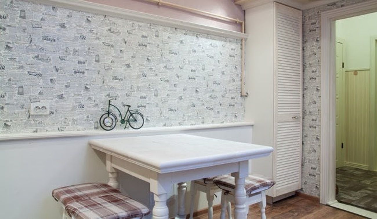 A room with a white table and two plaid chairs, a bicycle leaning against the wall, and a door leading to another room.