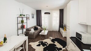 A modern living room with a sofa, coffee table, and a dining area with a white table and chairs. There is a kitchen area with a microwave and a cabinet. - Apartment Horodotska 4 (Lviv)