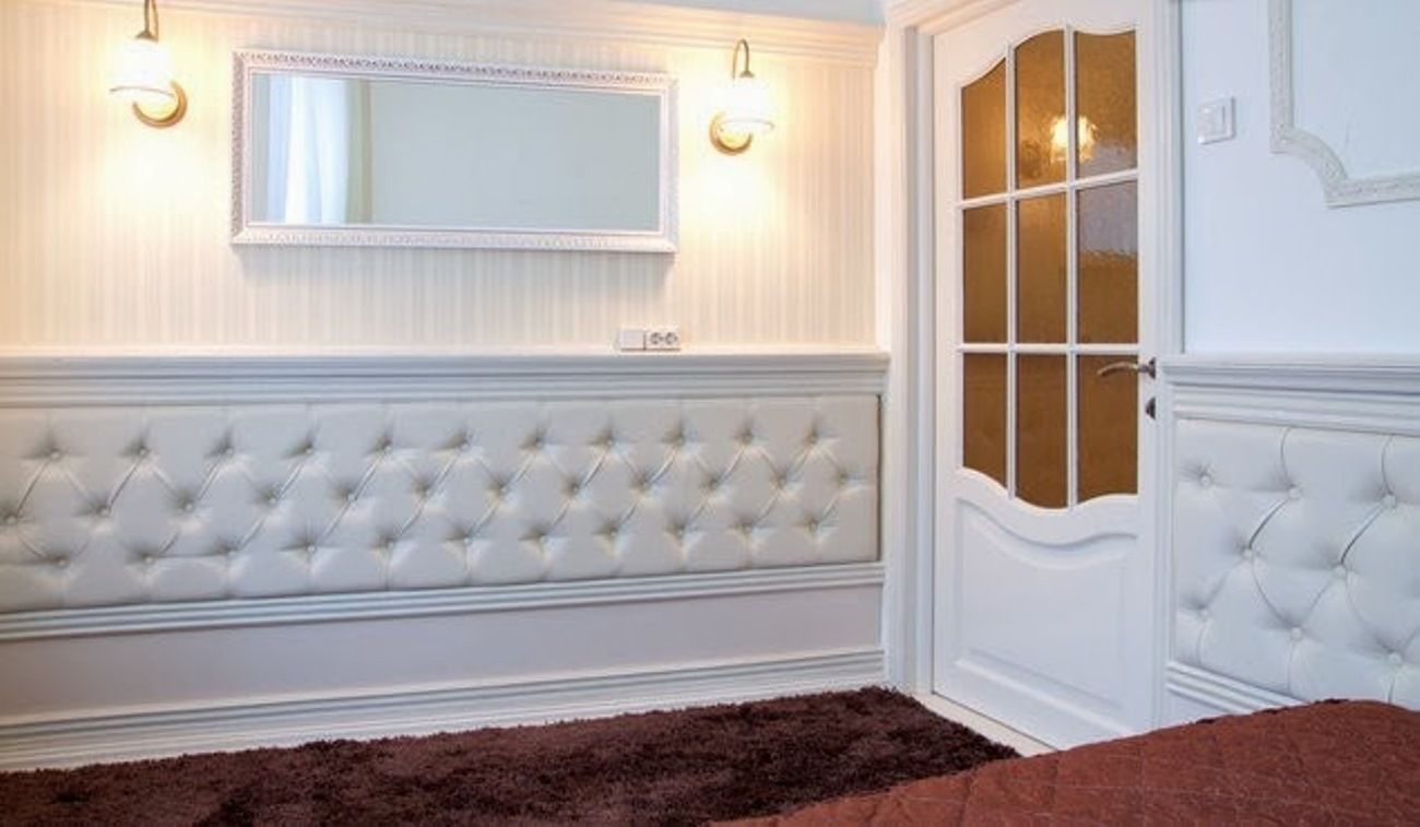 A room with a white tufted headboard, a large mirror, and a door with glass panels.