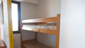 A bunk bed with two levels, a small wooden stool, and a window.