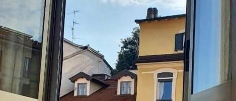 Una habitación con un ventanal grande, una cama con colcha estampada y vista a edificios cercanos.