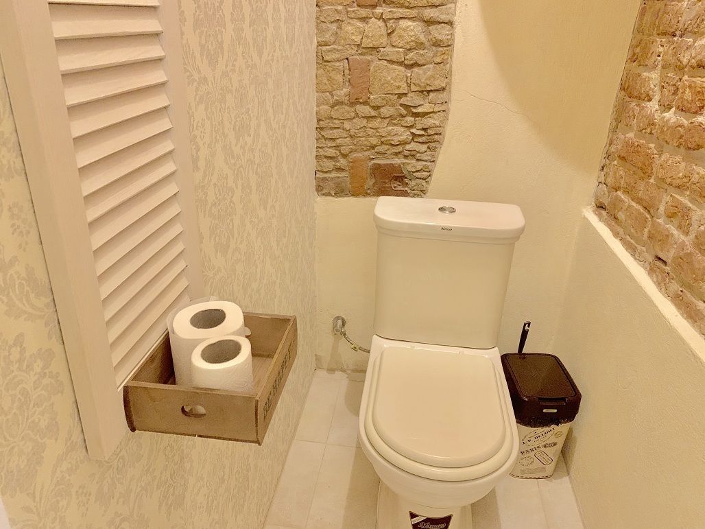 Un baño con un inodoro, una caja de madera con papel higiénico y un cubo de basura.